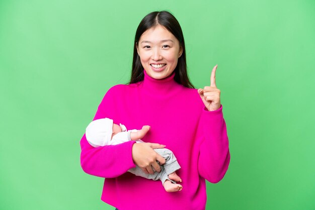 Young Asian woman with her newborn baby over isolated chroma key background pointing up a great idea