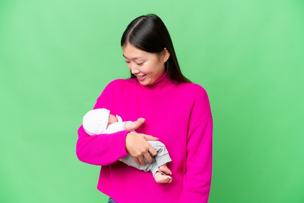 Young Asian woman with her newborn baby over isolated chroma key background with happy expression