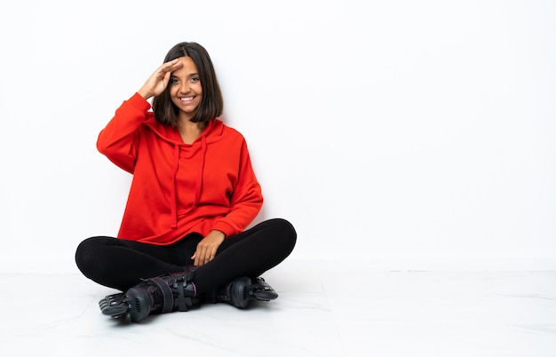 Young asian woman with roller skates on the floor saluting with hand with happy expression