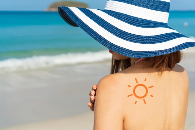 Young Asian woman with sun shape on the shoulder apply sun cream on her shoulder Summer on beach concept