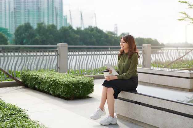 Young asian woman with tablet surfing in internet on bench park