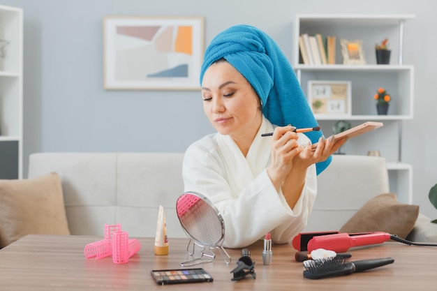 Young asian woman with towel on her head sitting at the dressing table at home interior applying eye shadows holding palette doing morning makeup routine beauty and facial cosmetics concept