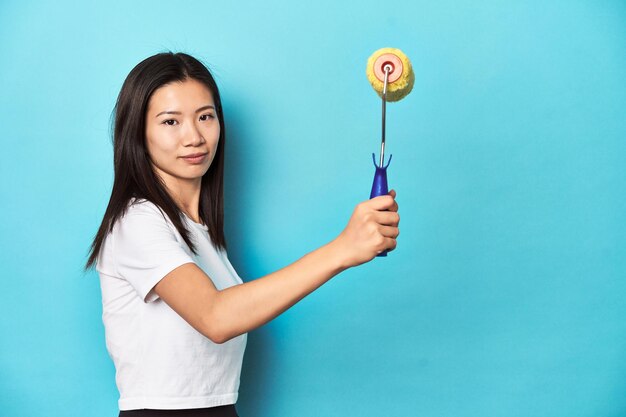 Young Asian woman with yellow paint roller studio shot