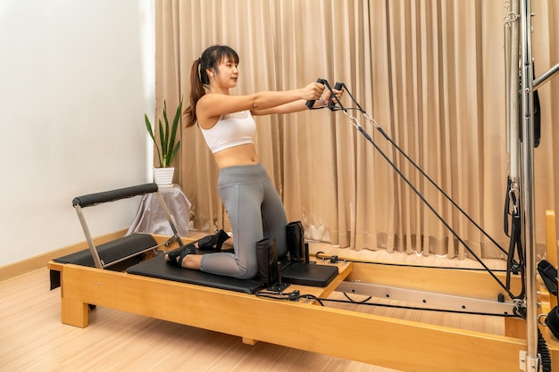 Photo young asian woman working on pilates reformer machine during her health exercise training