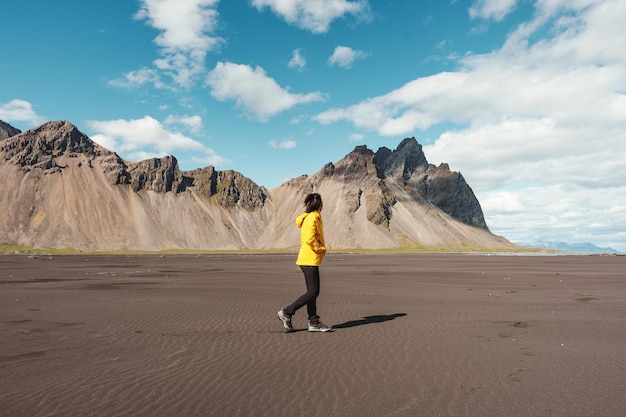 Young asian woman in yellow jacket standing on the beach with Vestrahorn mountain in viking village on Stokknes at Iceland