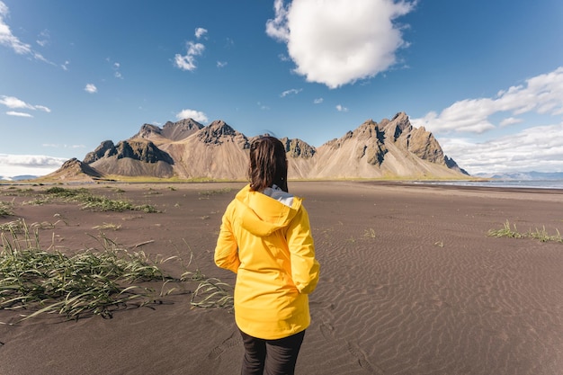 Young asian woman in yellow jacket standing on the beach with Vestrahorn mountain in viking village on Stokknes at Iceland