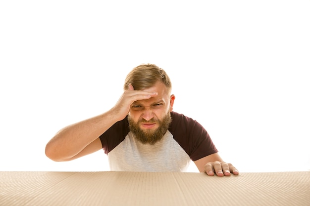 Young astonished man on biggest postal package isolated on white. Shocked male model on top of cardboard box looking inside.