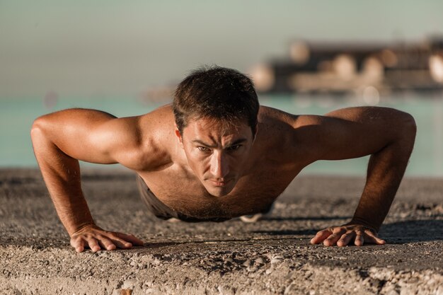 young athlete doing push-ups on the seashore