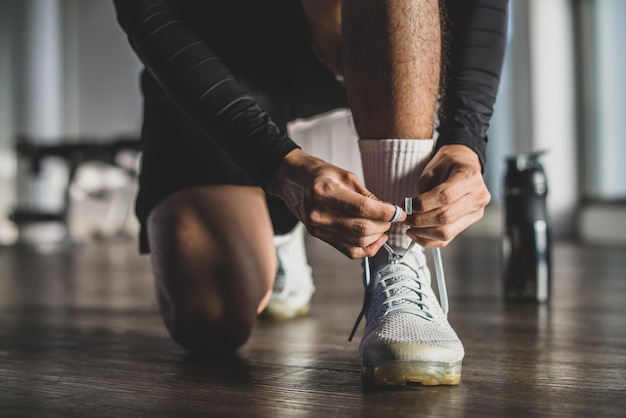 Young athlete wearing black sport wear tying shoelaces on white sports shoes before exercise in the gym