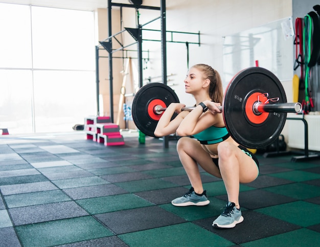 Young athlete woman in sportswear doing front squats with a barbell on the chest in the gym