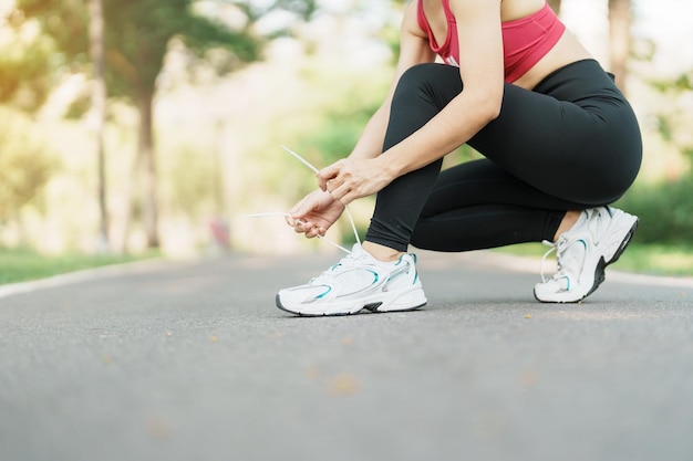 Young athlete woman tying running shoes in the park outdoor female runner ready for jogging on the road outside asian Fitness walking and exercise on footpath in morning wellness and sport concepts