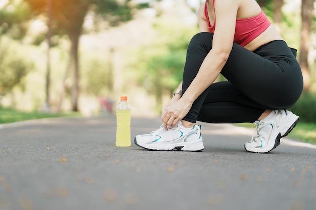 Young athlete woman tying running shoes with Energy Drink water female runner ready for jogging outside asian Fitness walking and exercise in the park morning wellness wellbeing and sport concepts