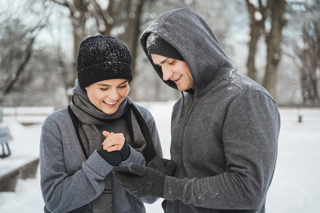 Young athletic couple are using smartphone during winter workout in snowy city park