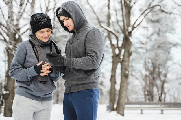 Young athletic couple are using smartphone during winter workout in snowy city park