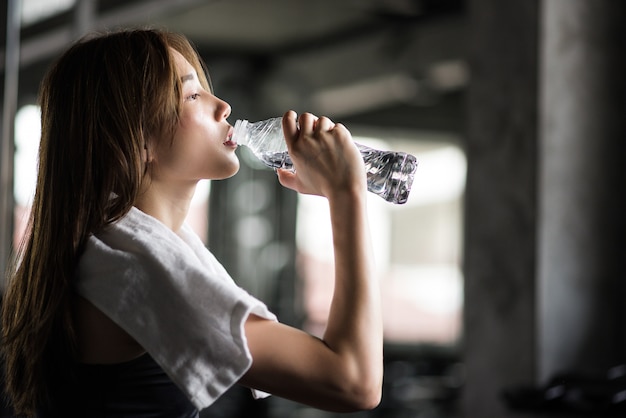 Young athletic fitness woman drinking water from bottle  in gym.