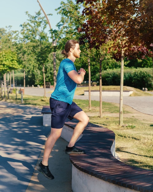 Young athletic guy in sports clothes doing exercising outdoors on sunny summer day