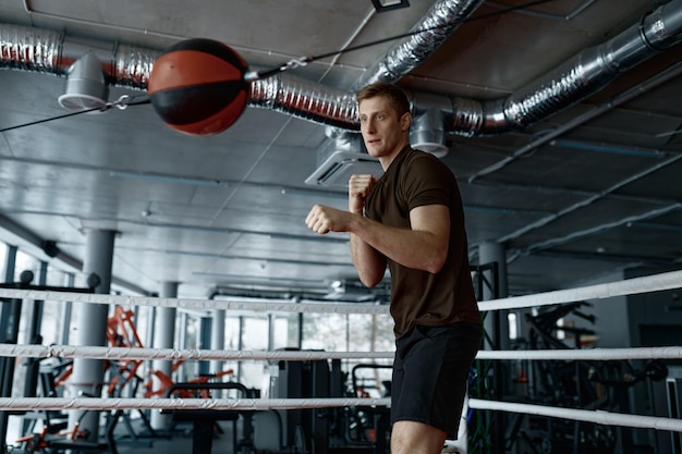 Young athletic man boxer strong fighter training with punching bag in gym ring preparing for training