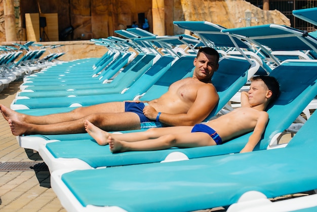 A young athletic man and his son are smiling happily and sunbathing on a sun lounger on a sunny day. Happy vacation vacation. Summer holidays and tourism.