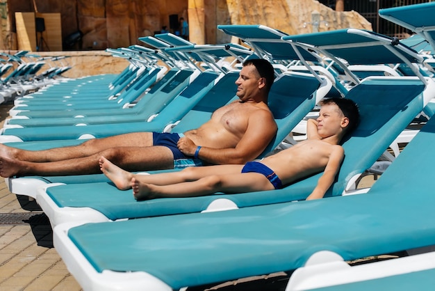 A young athletic man and his son are smiling happily and sunbathing on a sun lounger on a sunny day at the hotel Happy family vacation at a hotel in the resort Summer holidays and tourism