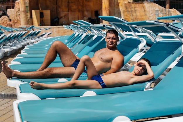 A young athletic man and his son are smiling happily and sunbathing on a sun lounger on a sunny day at the hotel Happy family vacation at a hotel in the resort Summer holidays and tourism