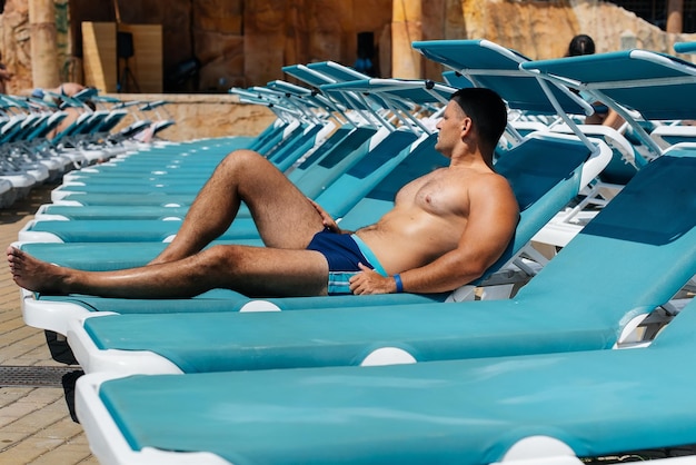 A young athletic man is smiling happily and sunbathing on a sun lounger on a sunny day at the hotel Happy family vacation at a hotel in the resort Summer holidays and tourism