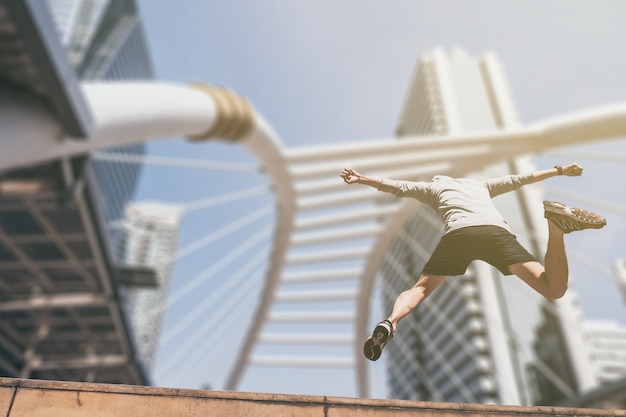 Young athletic man jumping while exercising on city bridge at the morning. 