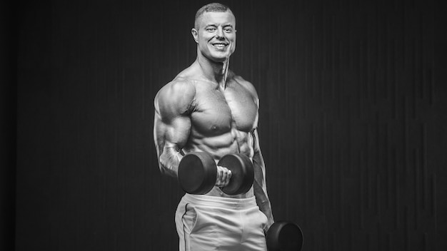 Young athletic man pumping up muscles in the gym at workout Sport and health care concept backgroun