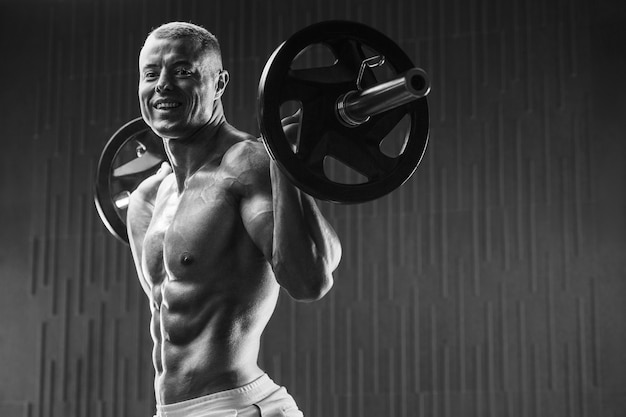 Young athletic man pumping up muscles in the gym at workout Sport and health care concept backgroun