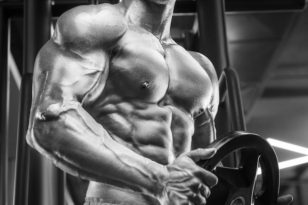 Young athletic man pumping up muscles in the gym at workout Sport and health care concept backgroun