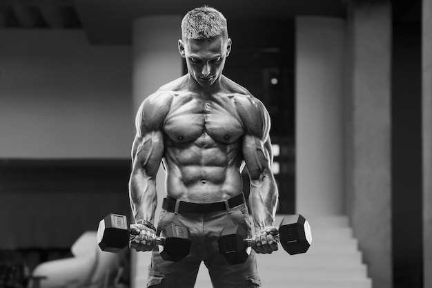 Young athletic man pumping up muscles in the gym at workout Sport and health care concept