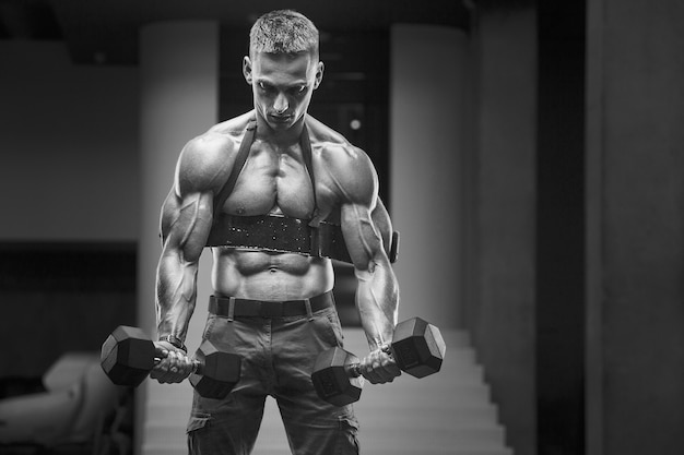 Young athletic man pumping up muscles in the gym at workout Sport and health care concept