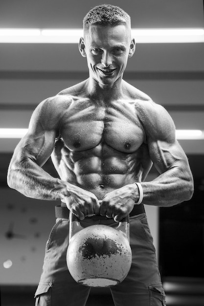 Young athletic man pumping up muscles in the gym at workout Sport and health care concept