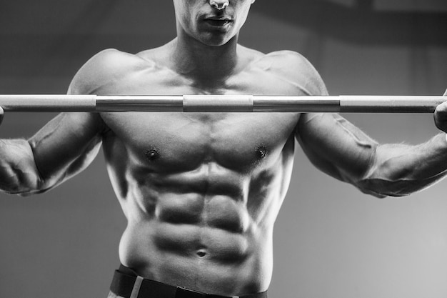 Young athletic man pumping up muscles in the gym at workout Sport and health care concept