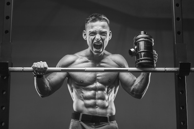 Young athletic man pumping up muscles in the gym at workout Sport and health care concept