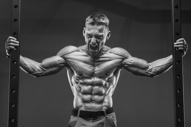 Young athletic man pumping up muscles in the gym at workout Sport and health care concept