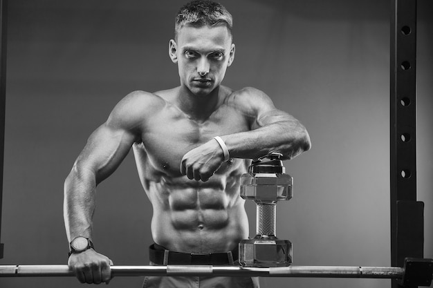 Young athletic man pumping up muscles in the gym at workout Sport and health care concept