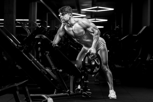 Young athletic man pumping up muscles in the gym at workout Sport and health care concept