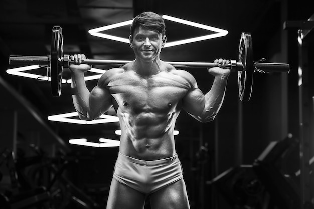 Young athletic man pumping up muscles in the gym at workout Sport and health care concept