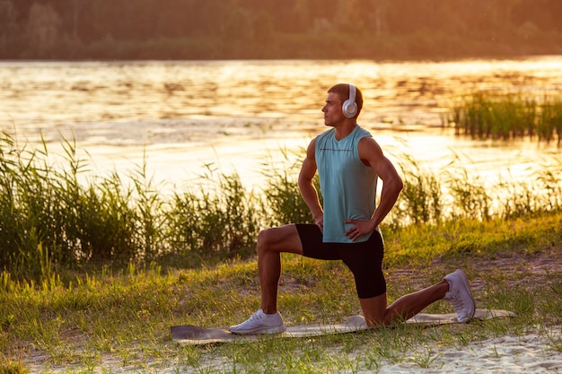 A young athletic man working out listening to the music at the riverside outdoors