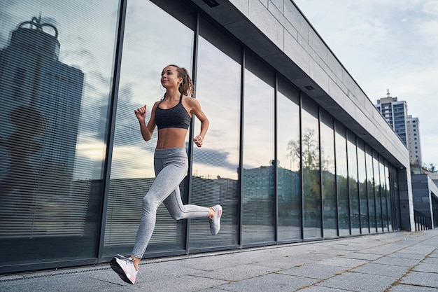 Young athletic woman running in the city shot of girl runner on the glass building background