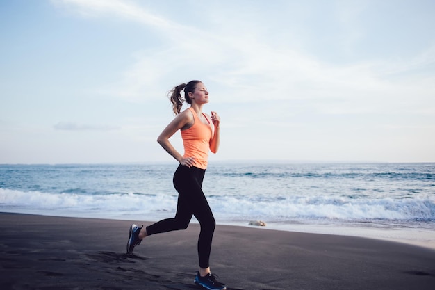 Young athletic woman in sportswear jogging on sea beach