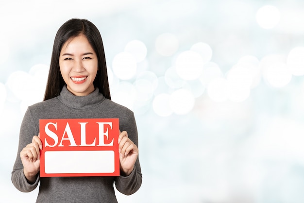 Young attractive asian woman holding sale signboard card showing for price tag