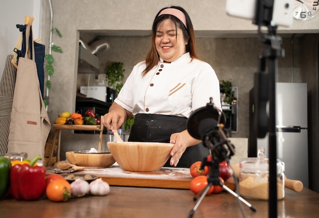 Photo young attractive asian woman is blogging for her kitchen channel about homemade pizza while streaming online for webinar masterclass lesson vlogger broadcasting live video online teaching cooking