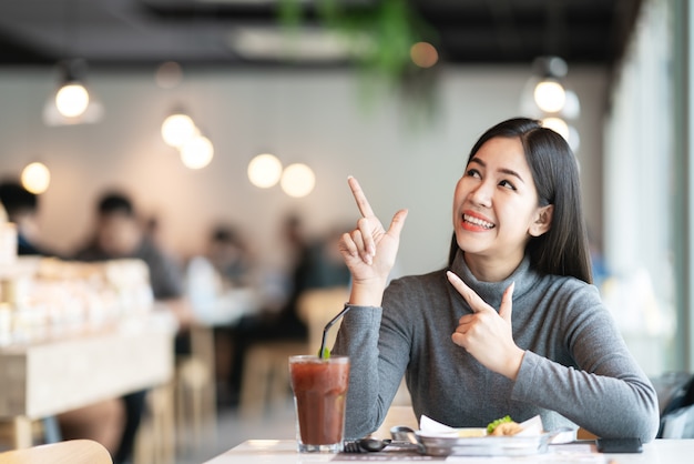 Young attractive asian woman pointing and look up above to side