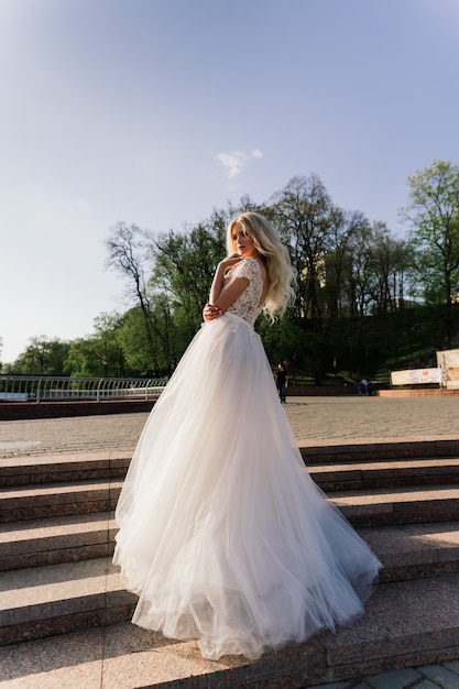 Young attractive blonde bride with curly hair walking in the park and smiling