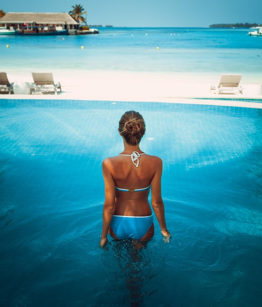 Young attractive blonde girl with perfect sport body in bikini on the tropical summer beach pool