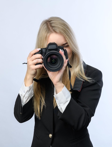 Young attractive blonde woman with modern DSLR cameras taking photo on white background