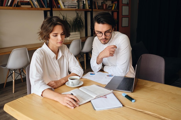 Young attractive business colleagues dreamily working together with laptop and papers in modern office