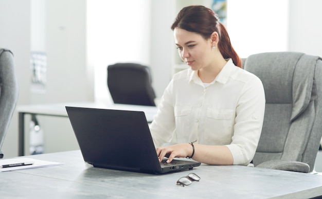 Young attractive business woman working in office smiling looking into laptop.