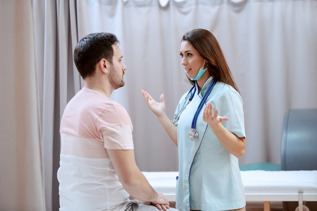 Young attractive Caucasian female doctor with stethoscope around neck talking to sick man.